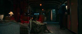 Movie still from “No One Gets Out Alive” (2021), directed by Santiago Menghini – A woman sitting on a chair in a living room; Wide shot, High angle