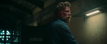 Movie still from “No One Gets Out Alive” (2021), directed by Santiago Menghini – A man with a long beard is standing in a dark room; Close Up shot, Low angle