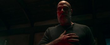 Movie still from “No One Gets Out Alive” (2021), directed by Santiago Menghini – A bald man with a beard and a red bandage on his hand; Close Up shot, Over the shoulder angle