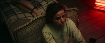 Movie still from “No One Gets Out Alive” (2021), directed by Santiago Menghini – A woman sitting on top of a couch with her head down; Close Up shot, High angle