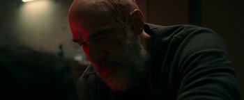 Movie still from “No One Gets Out Alive” (2021), directed by Santiago Menghini – A bald man with a beard and a scar on his face; Close Up shot, Over the shoulder angle