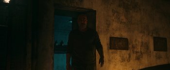 Movie still from “No One Gets Out Alive” (2021), directed by Santiago Menghini – A man walking in the dark in a dark room; Wide shot, Low angle