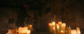 Movie still from “No One Gets Out Alive” (2021), directed by Santiago Menghini – A man standing in front of candles in a room; Medium shot, Low angle