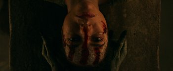 Movie still from “No One Gets Out Alive” (2021), directed by Santiago Menghini – A man with blood on his face is laying on a blanket; Extreme Close Up shot, Overhead angle