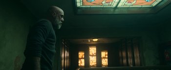 Movie still from “No One Gets Out Alive” (2021), directed by Santiago Menghini – A man standing next to a stained - glass window; Medium shot, Low angle