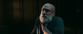 Movie still from “No One Gets Out Alive” (2021), directed by Santiago Menghini – An old man with a beard and a bloody nose; Close Up shot, Low angle
