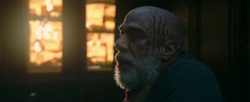 Movie still from “No One Gets Out Alive” (2021), directed by Santiago Menghini – An old man with a beard and some blood on his face; Close Up shot, Low angle