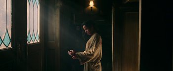Movie still from “No One Gets Out Alive” (2021), directed by Santiago Menghini – A woman standing in a dark room holding a cell phone; Medium shot, Low angle