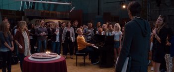 Movie still from “No Strings Attached” (2011), directed by Ivan Reitman – A man sitting at a piano in front of a group of people; Wide shot, Over the shoulder angle