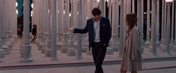 Movie still from “No Strings Attached” (2011), directed by Ivan Reitman – A man in a suit and tie standing in front of pillars; Medium shot, Over the shoulder angle