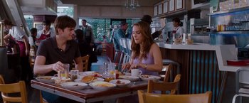 Movie still from “No Strings Attached” (2011), directed by Ivan Reitman – A woman sitting at a table with a plate of food in front of her; Medium shot, Over the shoulder angle