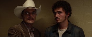 Movie still from “Nocturnal Animals” (2016), directed by Tom Ford – A man and a man in a cowboy hat standing next to each other; Close Up shot, Low angle