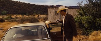 Movie still from “Nocturnal Animals” (2016), directed by Tom Ford – A man in a cowboy hat standing next to a car; Wide shot, Over the shoulder angle