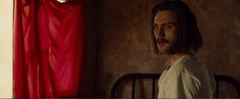 Movie still from “Nocturnal Animals” (2016), directed by Tom Ford – A man with long hair standing in front of a red curtain; Close Up shot, Over the shoulder angle