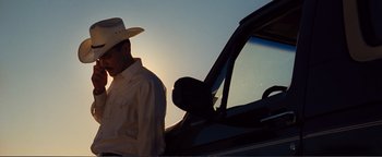 Movie still from “Nocturnal Animals” (2016), directed by Tom Ford – A man wearing a cowboy hat standing next to a car; Medium shot, Low angle