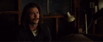 Movie still from “Nocturnal Animals” (2016), directed by Tom Ford – A man with long brown hair sitting in a dark room; Close Up shot, Over the shoulder angle