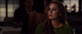 Movie still from “Nocturnal Animals” (2016), directed by Tom Ford – A woman with long red hair sitting in front of a group of people; Close Up shot, Over the shoulder angle