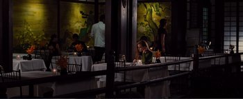 Movie still from “Nocturnal Animals” (2016), directed by Tom Ford – A woman sitting at a table in front of a painting; Wide shot, High angle