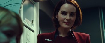 Movie still from “Non-Stop” (2014), directed by Jaume Collet-Serra – A woman in a red jacket is smiling for the camera; Close Up shot, Over the shoulder angle