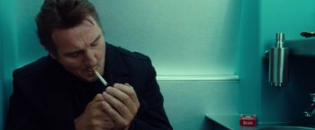 Movie still from “Non-Stop” (2014), directed by Jaume Collet-Serra – A man sitting down and smoking a cigarette; Close Up shot, Low angle