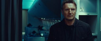 Movie still from “Non-Stop” (2014), directed by Jaume Collet-Serra – A man in a black jacket standing in an airplane; Close Up shot, Low angle