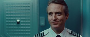 Movie still from “Non-Stop” (2014), directed by Jaume Collet-Serra – A man in a pilot's uniform smiling for the camera; Close Up shot, Low angle