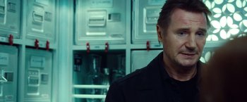 Movie still from “Non-Stop” (2014), directed by Jaume Collet-Serra – A person wearing a black shirt in a room; Close Up shot, Over the shoulder angle