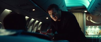 Movie still from “Non-Stop” (2014), directed by Jaume Collet-Serra – A man in a black shirt is sitting in a plane; Close Up shot, Low angle