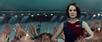 Movie still from “Non-Stop” (2014), directed by Jaume Collet-Serra – A woman standing in front of a group of people; Medium shot, Over the shoulder angle