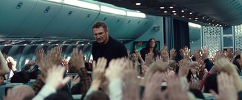Movie still from “Non-Stop” (2014), directed by Jaume Collet-Serra – A man standing in front of a group of people with their hands up; Medium shot, Over the shoulder angle
