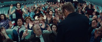 Movie still from “Non-Stop” (2014), directed by Jaume Collet-Serra – A crowd of people sitting and standing in front of a man; Wide shot, High angle