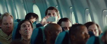 Movie still from “Non-Stop” (2014), directed by Jaume Collet-Serra – A man taking a picture with his cell phone while sitting on a plane; Medium shot, Over the shoulder angle