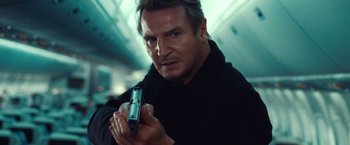 Movie still from “Non-Stop” (2014), directed by Jaume Collet-Serra – A man holding a gun while standing in a room; Close Up shot, Low angle