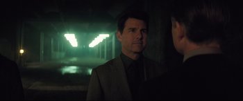 Movie still from “Mission: Impossible - Fallout” (2018), directed by Christopher McQuarrie – A man wearing a suit and tie standing in a dimly - lit room; Medium shot, Over the shoulder angle