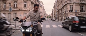 Movie still from “Mission: Impossible - Fallout” (2018), directed by Christopher McQuarrie – A man riding a motorcycle down the middle of the street; Medium shot, Low angle