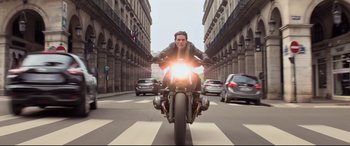 Movie still from “Mission: Impossible - Fallout” (2018), directed by Christopher McQuarrie – A man riding a motorcycle down a street; Wide shot, Low angle