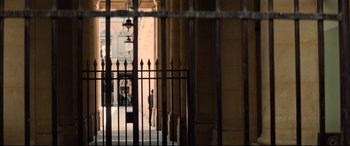 Movie still from “Mission: Impossible - Fallout” (2018), directed by Christopher McQuarrie – A man standing in front of a building behind a metal fence; Extreme Wide shot, High angle