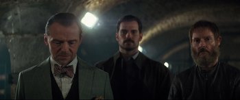 Movie still from “Mission: Impossible - Fallout” (2018), directed by Christopher McQuarrie – Two men in suits and ties in a dimly - lit room; Medium shot, Over the shoulder angle