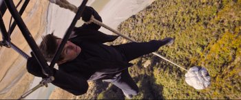 Movie still from “Mission: Impossible - Fallout” (2018), directed by Christopher McQuarrie – A man is hanging from a rope on the side of a building; Wide shot, Overhead angle