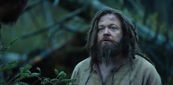 A man with a long beard is standing in the woods