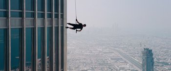 Movie still from “Mission: Impossible - Ghost Protocol” (2011), directed by Brad Bird – A man hanging from a rope on the side of a tall building; Wide shot, Low angle