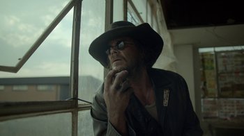 Movie still from “Oats Studios” (2017), directed by Neill Blomkamp – A man in a hat and glasses leaning against a window; Close Up shot, Low angle