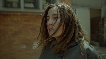 Movie still from “Oats Studios” (2017), directed by Neill Blomkamp – A woman with dreadlocks standing in front of a brick wall; Close Up shot, Over the shoulder angle