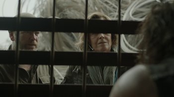Movie still from “Oats Studios” (2017), directed by Neill Blomkamp – A woman looking through a fence at a building through bars; Close Up shot, Over the shoulder angle