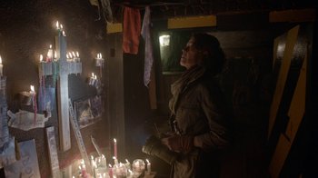 Movie still from “Oats Studios” (2017), directed by Neill Blomkamp – A woman standing next to a bunch of lit candles; Medium shot, Over the shoulder angle