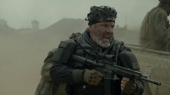 Movie still from “Oats Studios” (2017), directed by Neill Blomkamp – An old man with a beard is holding a rifle; Medium shot, Over the shoulder angle