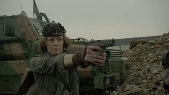 Movie still from “Oats Studios” (2017), directed by Neill Blomkamp – A woman holding a gun while standing in front of a truck; Medium shot, Over the shoulder angle