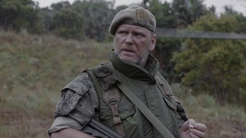 Movie still from “Oats Studios” (2017), directed by Neill Blomkamp – A man wearing a hat and holding a rifle; Close Up shot, Over the shoulder angle