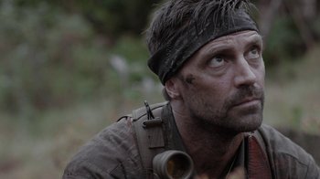 Movie still from “Oats Studios” (2017), directed by Neill Blomkamp – A person wearing a hat and looking to his left; Close Up shot, Over the shoulder angle