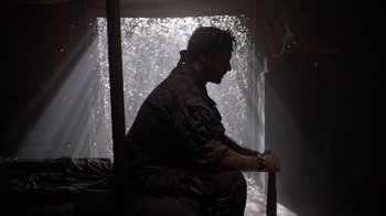 Movie still from “Oats Studios” (2017), directed by Neill Blomkamp – A man sitting on a bench in a room; Medium shot, Low angle